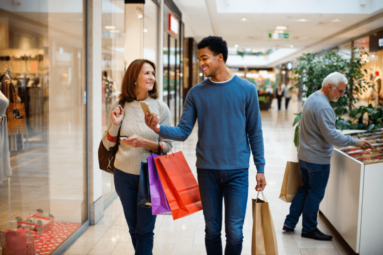 Three shoppers carrying bags and browsing products in a mall